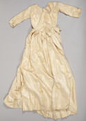 Older girl's ivory silk twill dress with elbow-length sleeves decorated with three blue silk-covered buttons at cuffs. Embellished at waistline with many silk petals originally edged with fine blue silk ribbon.