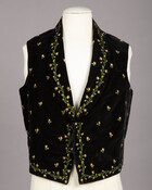 Child's black velveteen waistcoat with three-dimensional floral embroidery of rosebuds across front and bordering front and hem. Garment has rolled collar and covered buttons.