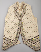 Child's ivory waistcoat with pink, green, and purple embroidery and sequins throughout. Leaf and floral motif around edges and pockets. Circle and triangle motif across front. Waistcoat has six buttons and two pockets.