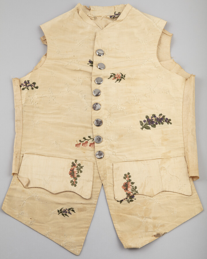 Young child's unfinished ivory floral silk waistcoat. Closes in front with eight metal buttons not original to garment. Two pocket flaps on front. Made from older fabric from the mother's dress.