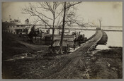 View of a pontoon bridge on the James River in Virginia during the American Civil War. Soldiers can be seen standing guard along with several supply boats and an anchored steamship. One boat visible in the image has been identified as the "A. Dornfeld."