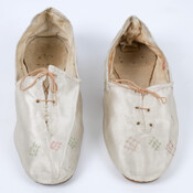 Pair of women's satin slippers. Both shoes lace at the front with three sets of eyelets. Light green and pink embroidery was likely added at a later date.