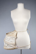 Hand-sewn pannier panel to be worn on one side of hip under a skirt to provide shape. Semi-circular hoops with stiff boning. The name "Hollyday" is written in pencil on the bottom edge. Traditionally, two panniers would be worn, one on each hip.