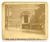 A view of the entrance of Taney House located on the north side of Lexington Street, east of St. Paul Street in Baltimore, Maryland. Four people are seen on the periphery of the photo with two clad in long skirts. The description at the bottom of the photo reads, "Taney House - N. side of…