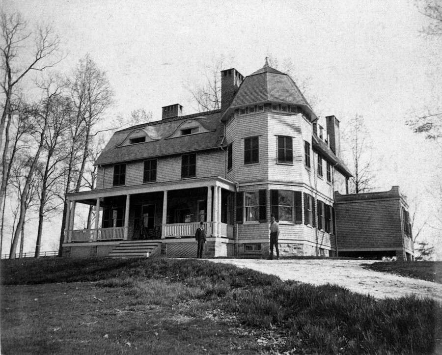 View of the main house on the Kedleston estate, located in Ruxton, Maryland. Two men stand in front of the building. Designed by John Appleton Wilson and his cousin William Thomas Wilson, this 18-acre estate was the country seat of Richard Curzon Hoffman (1839-1926), a Baltimore stock broker and railroad official.