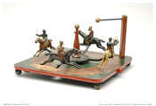 Four racers on horses attached to a spinning center piece. Wood base is painted to look like a race track. Red knob on the base is pulled to start toy.