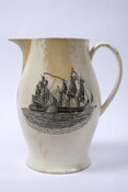 Creamware pitcher with bulbous form and black transfer printed designs on front and sides. The front bears the motto, "SUCCESS TO THE INFANT NAVY OF AMERICA" inside a wreath. One side features images of the shipbuilding process from tree to finished ship with words of a poem beginning, "Our Mountains are cover'd with Imperial Oak."…