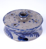 Stoneware inkwell with blue glazed designs. Inscribed on top and bottom. Four small pen holes and one large central opening. Star ornamentation of glaze and flower and leaf motif along side of inkwell. The bottom is clear-glazed.