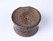 Salt-glazed stoneware sander, iron-oxide dip around exterior, round, flat-top with holes. Sanders held powdered gum sandarac, which, when sprinkled on paper, prevented ink smearing. Strictly an eighteenth and early nineteenth-century form, stoneware potters rarely manufactured sanders by 1825.