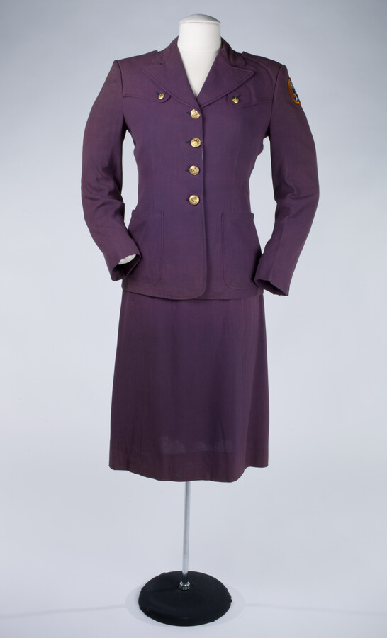 World War II Air Warning Corps woman's uniform. The uniform is comprised of a purple wool single-breasted jacket with gold buttons and a matching skirt. Red, white, and blue patch on the proper left sleeve reads "AWC."