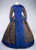 Figured silk or jacquard-woven morning wrapper comprised of a bronze and blue floral patterned fabric with wide blue trim throughout. The fabric of the dress dates to the previous decade. Two front pockets appear on the skirt, which is common for this type of informal garment.