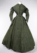 Lady's green corded ribbed silk dress with high neckline and full-length two-piece coat sleeves. The fabric is printed to appear as silk moire. Trimmed with black lace from shoulder to waist and white lace at cuffs. Embellished with black braided cord accents on bodice and wrists. Dress closes with a row of 10 hook-and-eye closures…