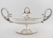 Silver covered tureen on an ovular pedestal, embellished with a beaded border on base and edge of lip. There are two handles in the shape of serpents and two decorative snake heads and the visage of a bearded man on either side. The lid has a serpent designed handle. This silver tureen was given to…