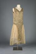 Ivory silk chiffon dress with a tape-lace skirt. The dress's bodice and panels are heavily beaded with silver-core glass and metal beads.