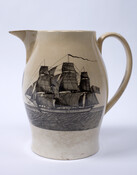 Creamware pitcher manufactured by Herculaneum Pottery in Liverpool, England. On one side is a black transfer print of a ship flying the American flag. On the opposite side, the motto "PEACE, PLENTY AND INDEPENDENCE" is displayed in an oval medallion that is flanked by female figures holding cornucopias, a cannon, battle flag, and spread-wing eagle.…