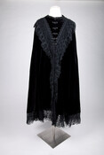 Full-length black velvet cape embellished with black lace trim at collar and hem. Closes in front with five clasps.