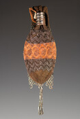Miser purse crocheted with brown and orange purse silk and steel cut beads in a striped design of chevrons and paisley motifs. Pair of silver metal rings slide to close opening. Squared-off end features a fringe-like lattice attachment worked with steel beads. Rounded end has a looped tassel made up of steel-cut seed beads and…