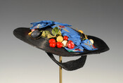 Black leghorn style straw hat with low crown and very wide brim. Embellished with blue floral silk brocade bow and a wreath of faux fruit.