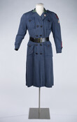 Woman's WWII Red Cross Motor Service uniform that includes a blue dress (a) with folded collar and notched lapels with a double breasted front that closes with eight black buttons. The dress has pockets with buttoning flaps on both sides of chest and hips and a proper left sleeve that bears an embroidered patch reading…