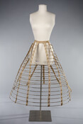 Thomson cage crinoline made in France. The supportive undergarment consists of 11 twill tapes for holding 18 steel wires in place, which are further held into place by brass tooth on tape. On both sides, wires are connected by joints that contract and invert, allowing for easier mobility.