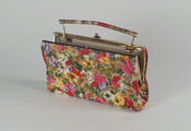Rectangular handbag covered in vibrant floral printed silk with matching fabric handle with brass trim. Lined with pink vinyl. Small mirror contained within interior pocket.
