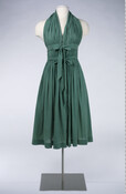 Green cotton wrap-tie halter dress made by Townley Clothes and designed by Claire McCardell (1905-1958). One single piece of fabric extends from one side of the waist around the neck to the other side of the waist. The shape of the garment is given by the bunching of the fabric created by the effect of…