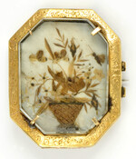 Mourning brooch with ornate gold frame featuring a hairwork image of a floral bouquet in a vase. The obverse side shows a miniature portrait of a female member of the Wilkins family. Owned by Georgia Bell Spalding Wilkins (186?-1952) who was a resident of Baltimore and Carroll Counties.