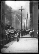 A view of the fire at the A. Hoen & Company building located at 300-316 East Lexington Street in Baltimore, Maryland. Firefighters work to extinguish the blaze while spectators observe. A horse-drawn fire truck is on the street, while water towers pour water onto the building. The building was heavily damaged in the fire and…