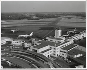 View of a terminal and several airplanes at Friendship International Airport, located nine miles south of Downtown Baltimore in Anne Arundel County, Maryland. Dedicated by President Harry S. Truman on June 24, 1950, the airport was named after the nearby Friendship Methodist Church. In 1972, the Maryland Department of Transportation purchased the airport from Baltimore…