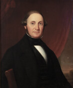 Seated half-length portrait shows Colonel Alfred Sellman. He wears a black coat with white shirt and black stock. His left arm rests over back of a red-upholstered side chair as he sits in front of a draped red curtain.