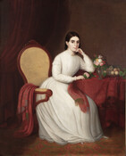 Full-length portrait shows Mary Ann Sellman Ingleheart seated upon a yellow upholstered Victorian armchair. She is pictured wearing a long white dress with a high neck and full-length sleeves, accented with a gold brooch pinned at her collar and gold tassel earrings. Her brown hair is pulled back behind her neck. Her right hand and…