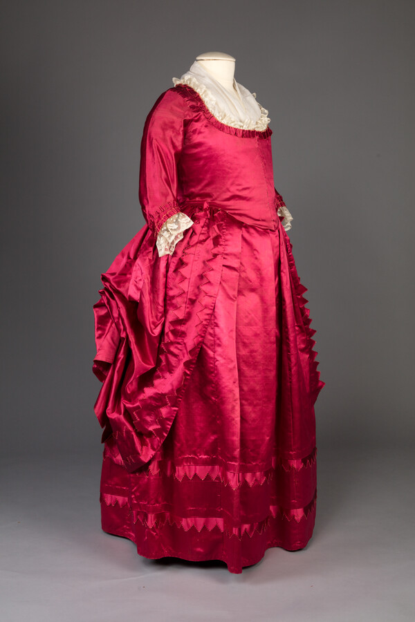 Fuchsia silk satin open front gown and matching petticoat with pinked ruching around neck and sleeves. Interior of skirt has loops and ties to drape into a polonaise style.