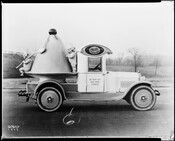 A Hendler's ice cream truck featuring the company's Kewpie mascots beside a large bowl of ice cream. On the roof is the Hendler's logo with the company's catch phrase, "The Velvet Kind." The door reads "On Your Way Take Home A Brick." The negative is dated 1923 with the signature "Leopold" in the lower left…