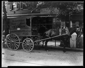 A Hendler Creamery horse-drawn ice cream cart. The cart is stopped on a cobblestone street in front of a tobacco shop in Baltimore, Maryland. The side of the cart reads "The Velvet Kind - Pasteurized - Homogenized - Ice Cream - Baltimore - Hendler Creamery."