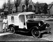 A Good Humor driver stands beside his truck in a northern Baltimore, Maryland, neighborhood. The side of the truck reads "Good Humor Ice Cream 10¢ Each - Coconut - Toasted Almond - Chocolate Covered - Buy Them Here."