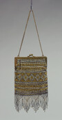 Loom-woven handbag beaded with steel and brass beads in a geometric diamond design. Purse is lined with gold silk taffeta and opens with a brass frame decorated with an embossed floral vine and a twin knob closure. Bottom fringe hand-woven in a lattice pattern with falling fringes. Made in France.
