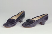 Pair of black leather shoes with square toe and low stacked heel. Embellished with bow and beadwork.