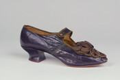 Brown kid leather shoe with pointed toe and button strap adjustment. Embellished with brown satin and bead trim on toe. Likely used as part of a costume as donor was a costume shop owner.