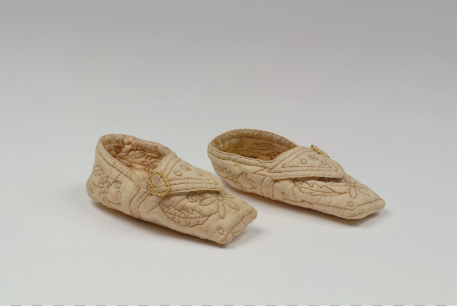 Pair of infant's white cotton quilted slippers. Floral embroidery sewn with brown cotton thread. Each shoe embellished with small gold buckle.