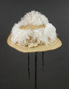 Cream horsehair hat with a large flat brim, which is trimmed with pink chiffon and artificial pink roses and green leaves. Pink ostrich feathers attached around the hat crown and left side. The light pink plumes have faded, with a tinge of the original pink visible on the underside of the plumes.