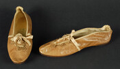 Lady's brown kid leather shoes. Tops laced with beige silk ribbon and sewn with beige silk braid with looped fringe. Edges bound with beige silk ribbon. Side seam and back seams covered with same ribbon, nine tassels decorate top of shoe. Soles of suede and polished leather. Lined with white linen. From the personal effects…