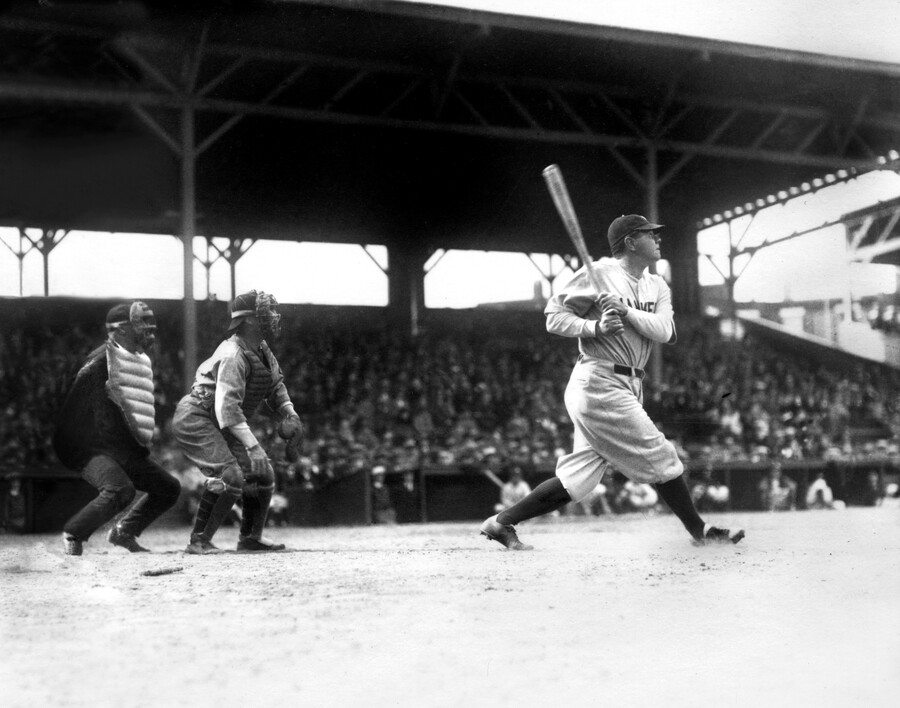 View of Babe Ruth at bat, with a crowd filling the stands behind him at the old Oriole Park. Ruth is wearing a New York Yankees uniform.
