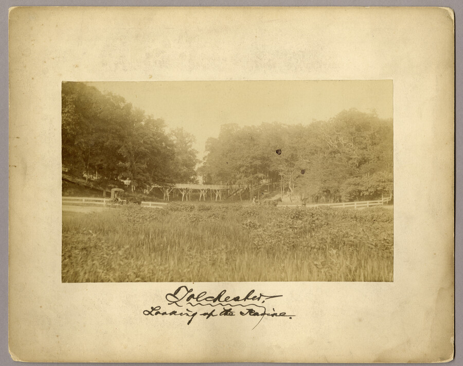 View of a road and railroad bridge in Tolchester, Maryland. Two horse carriages can be seen driving down the road. Tolchester was the site of the Tolchester Beach Amuseument Park, which consisted of a bathing beach, amusement park, racetrack, and hotel, and was in operation from 1877 to 1962. The Kent County park was a…