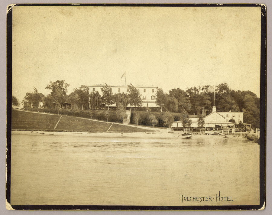 View of the Tolchester hotel from the Chesapeake Bay. Boats can be seen at the dock. The hotel was part of the the Tolchester Beach Amusement Park located in Kent County, Maryland. The park also consisted of a bathing beach, amusement park, and racetrack, and it was in operation from 1877 to 1962. It was…
