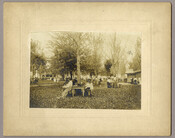 A view of people sitting at tables and standing on the picnic grounds of the Tolchester Beach Amusement Park in Tolchester, Maryland. The Kent County park consisted of a bathing beach, amusement park, racetrack, and hotel, and was in operation from 1877 to 1962. It was a popular vacation destination for Baltimoreans as it was…