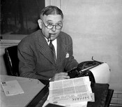 Portrait of American writer H. L. Mencken seated at a typewriter and smoking a cigar on his 60th birthday.