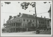 View of the Custom House located on Water Street in Chestertown, Maryland. A large porch extends from the side of the house, while a figure stands on the sidewalk with a hand on their hip. Built in 1746, the Custom House was the residence of Thomas Ringgold IV, an attorney and one of the most…
