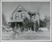Portrait of John Fagan Ernest with his wife, Eliner Reynolds Ernest, and their child, John Reynolds Ernest, standing in front of their house in Sassafrass, Maryland. The child is holding hands with the family's nurse Hozana Cristy. Bell Jane Cristy, the family's cook, stands by the back fence on the left, slightly blurred. Verso transcription:…