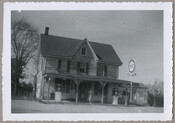 Exterior view of the general store run by the Lesage family, located at the corner of Route 298 and Porters Grove-Melitota Road in Melitota, Maryland. A woman stands on the porch of the building.