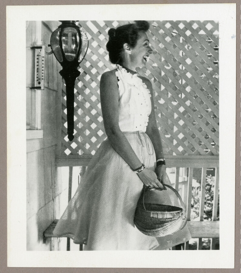 Undated photograph of American fashion designer Claire McCardell standing on a porch and holding a basket.